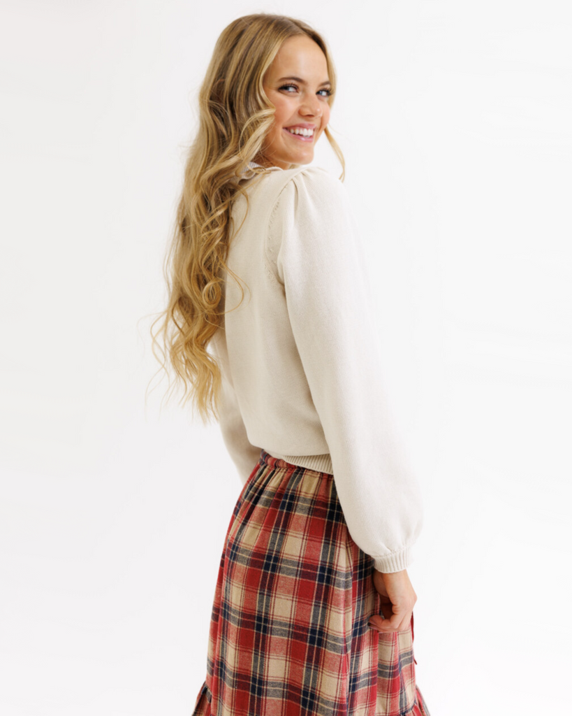 Woman wearing a cream colored sweater with a plaid skirt on a white background