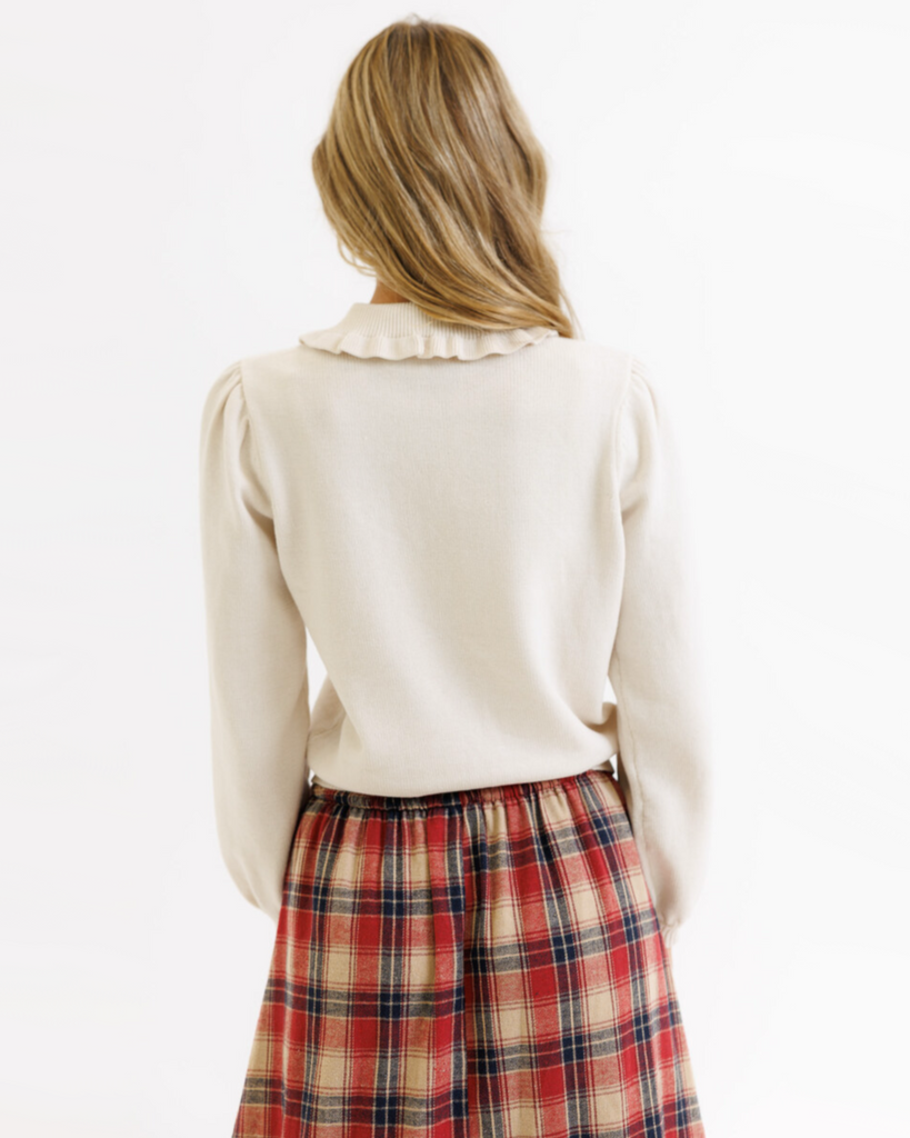 Woman wearing a cream colored sweater with a plaid skirt on a white background