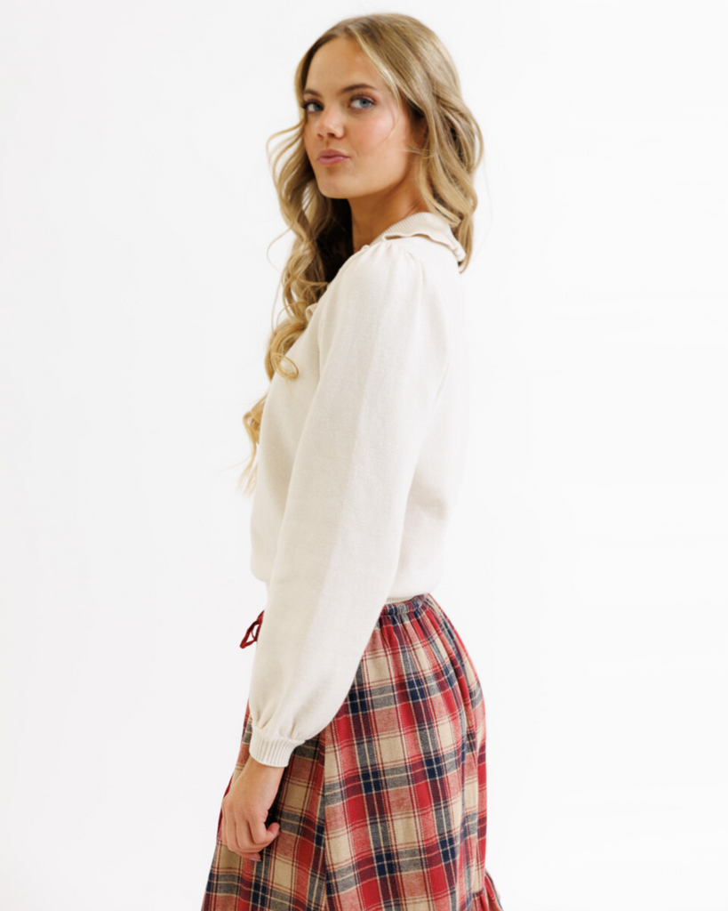 Woman wearing a cream colored sweater with a plaid skirt on a white background