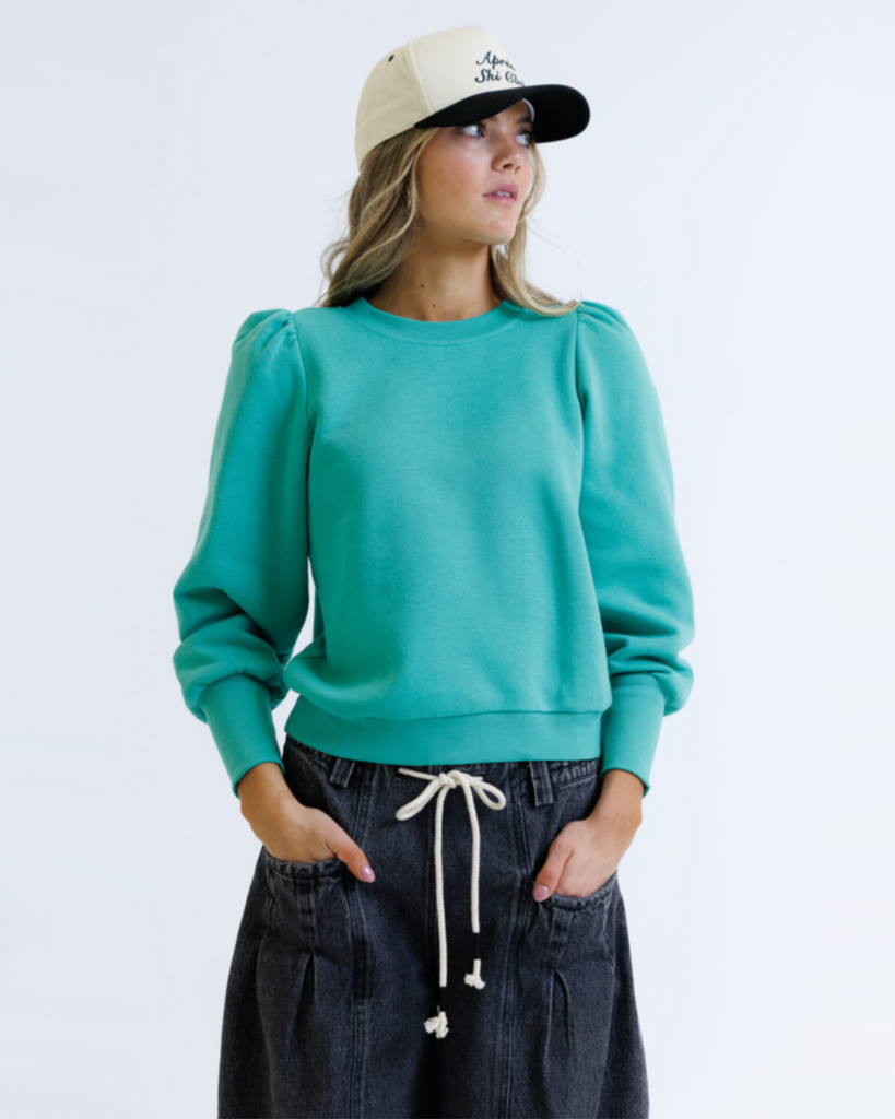 Woman wearing a teal sweater and beige cap on a white background