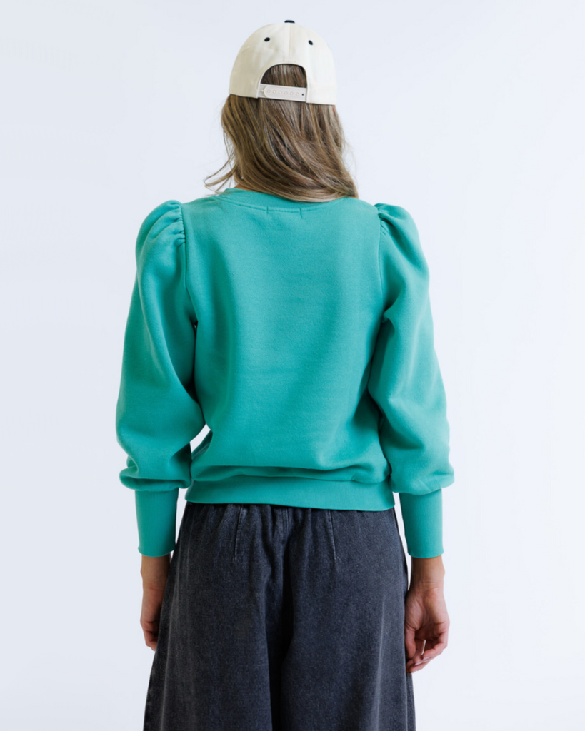 Woman wearing a teal sweater and beige cap on a white background