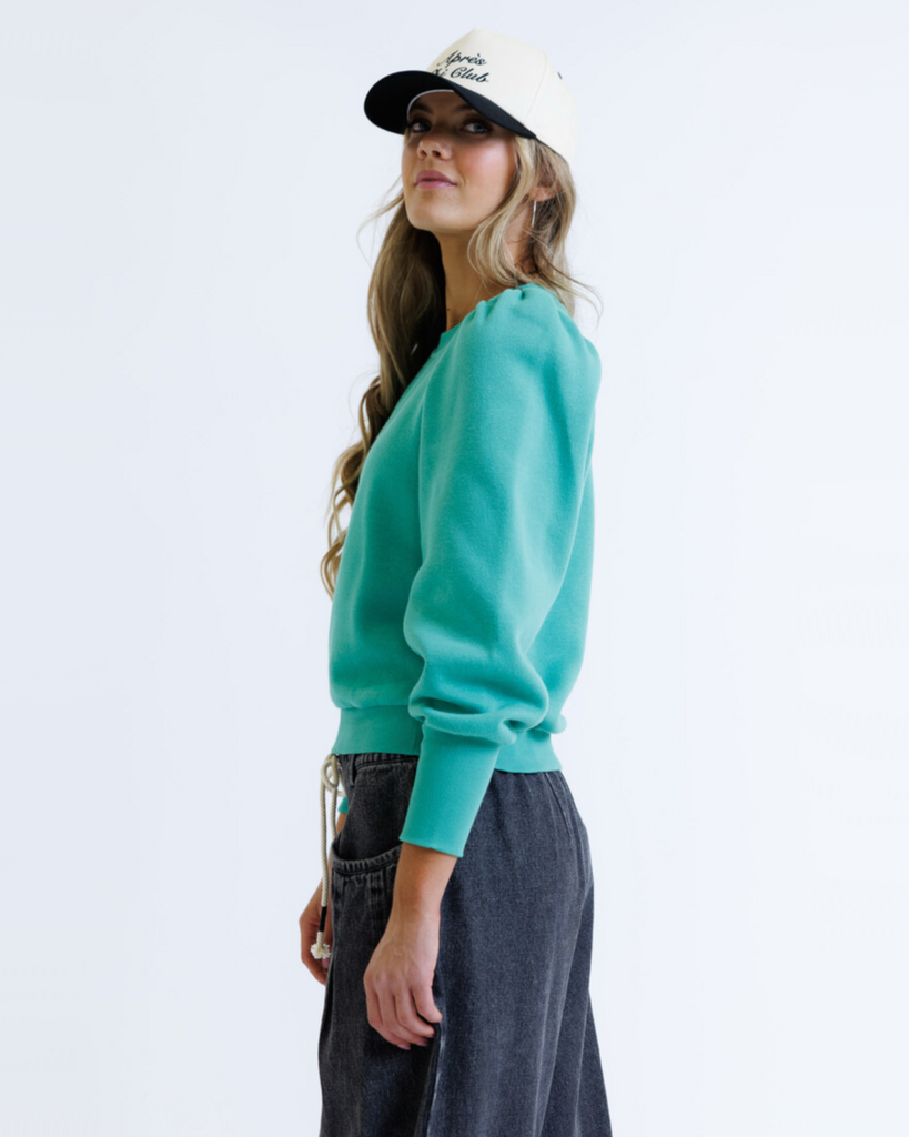Woman wearing a teal sweater and beige cap on a white background