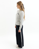 Woman wearing a gray sweater with black embroidered text that says 'bonjour' and black pants on a white background