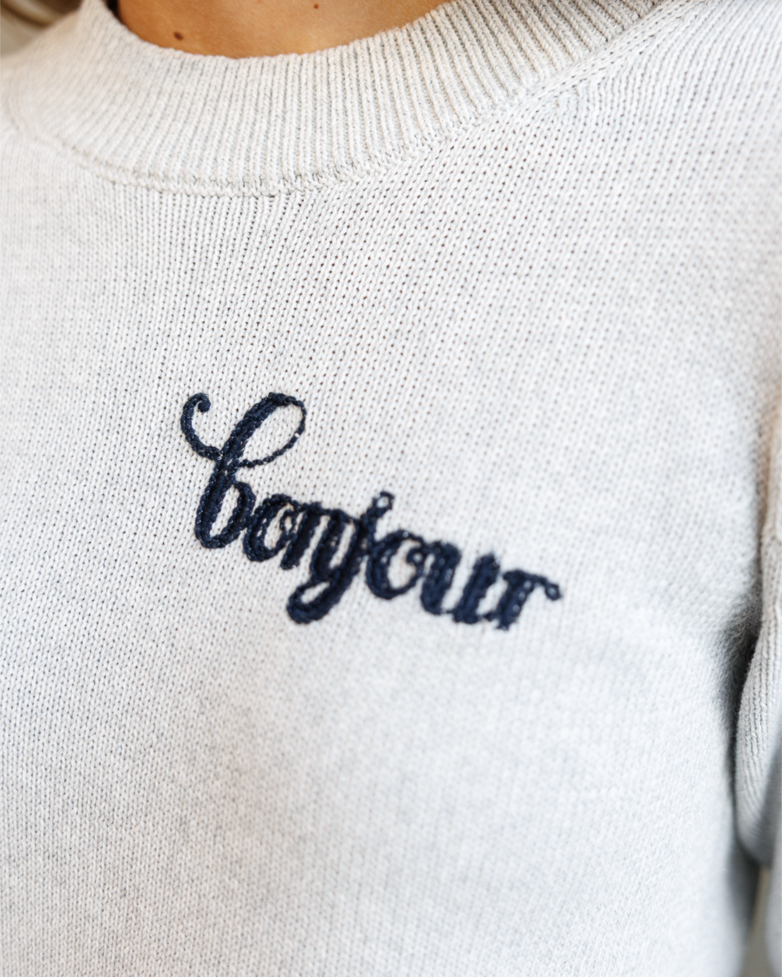 Close-up of a gray sweater with black embroidered text that says 'bonjour'