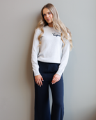 Woman wearing a gray sweater with text and dark pants against a plain background