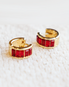 Gold hoop earrings with red gemstones on a white textured background