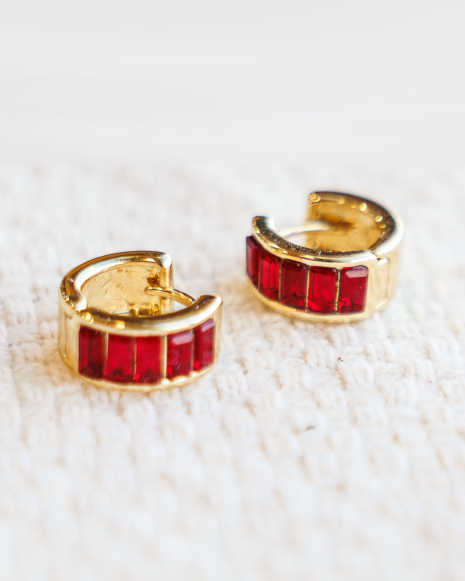 Gold hoop earrings with red gemstones on a white textured background