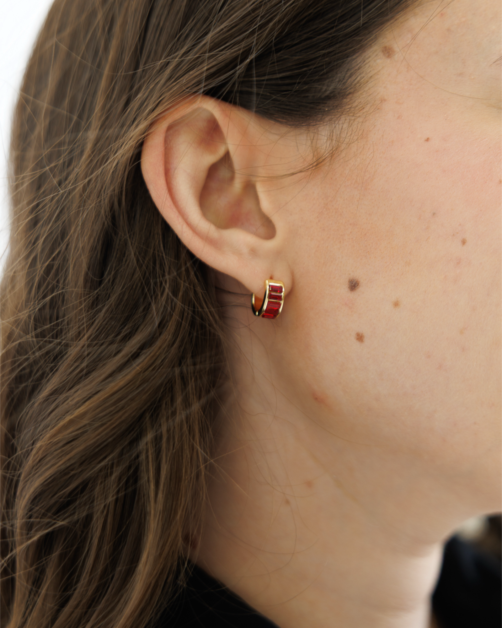 Close-up of a woman wearing a small hoop earring with red gemstones