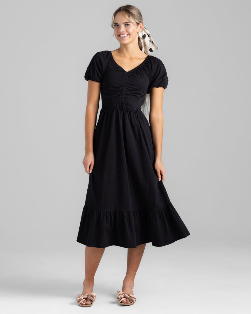 Model wearing a black short sleeve v-neck midi-length knit dress.