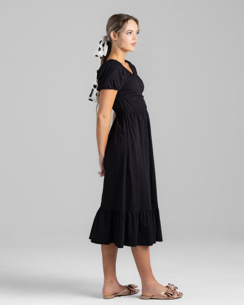 Model wearing a black short sleeve v-neck midi-length knit dress.