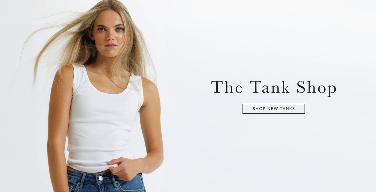A woman wearing a white tank top and blue jeans stands against a plain white background, with the text 'The Tank Shop' and a 'SHOP NEW TANKS' button on the right side.