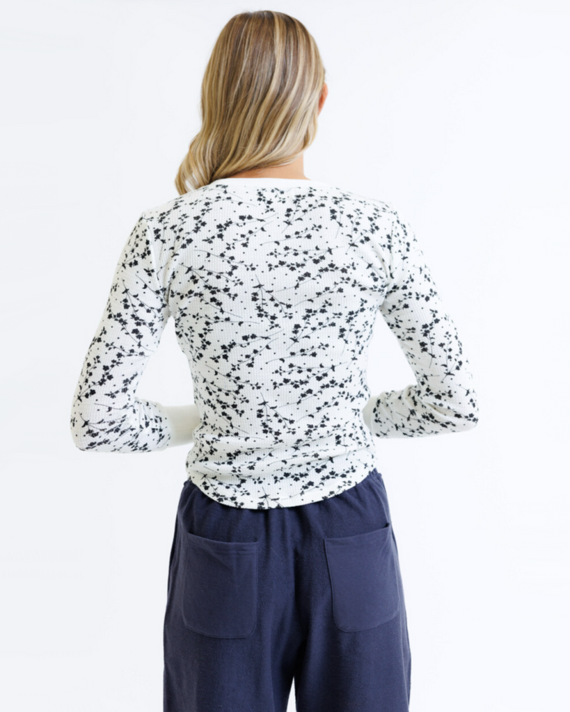 Woman wearing a white long-sleeve top with black speckles and navy pants on a white background