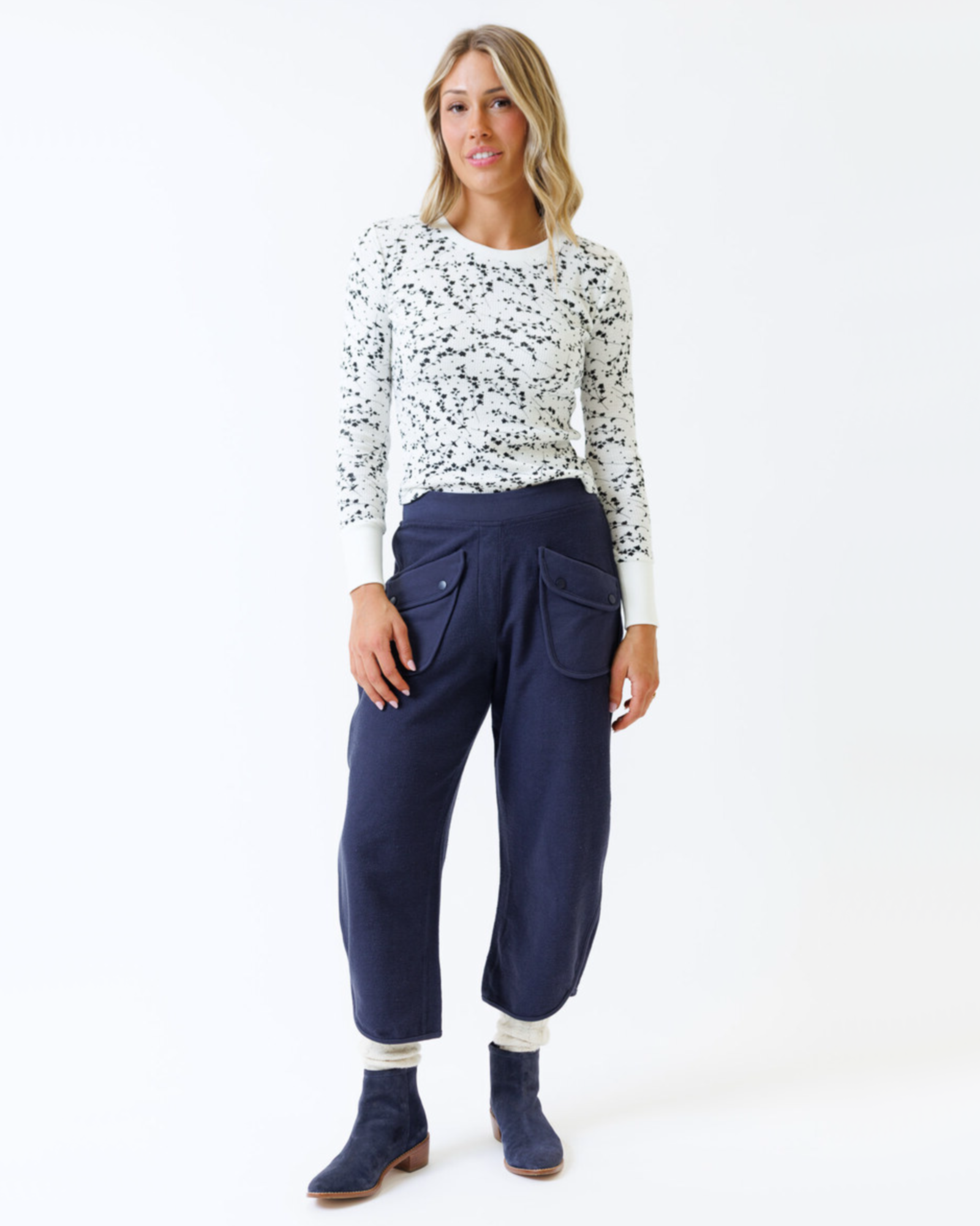 Woman wearing a white long-sleeve top with black speckles and navy pants on a white background
