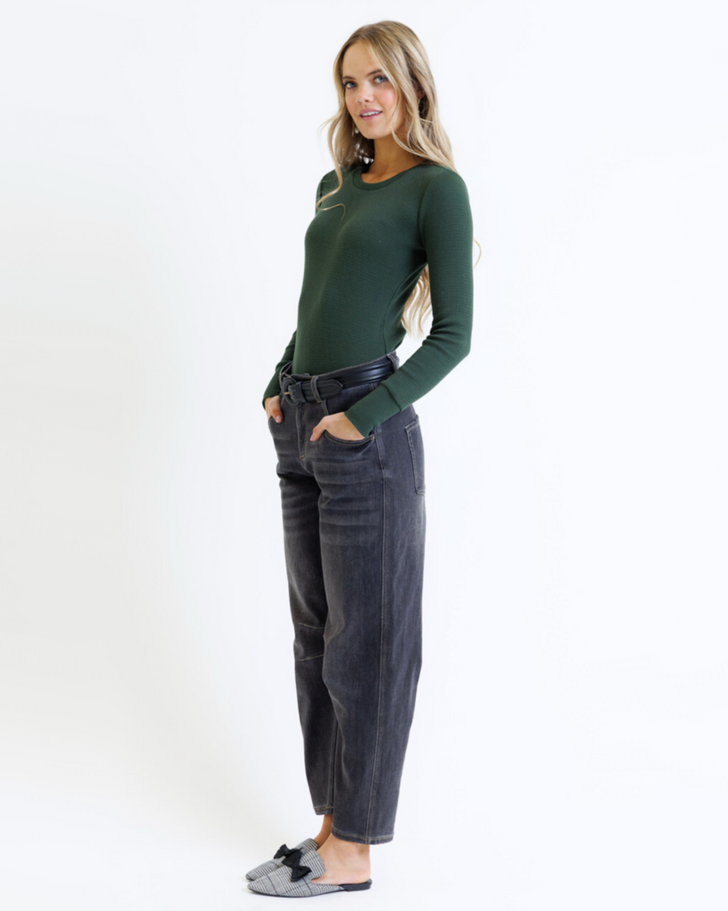Woman wearing a green long-sleeve top and dark jeans on a white background