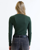 Woman wearing a green long-sleeve top and dark jeans on a white background