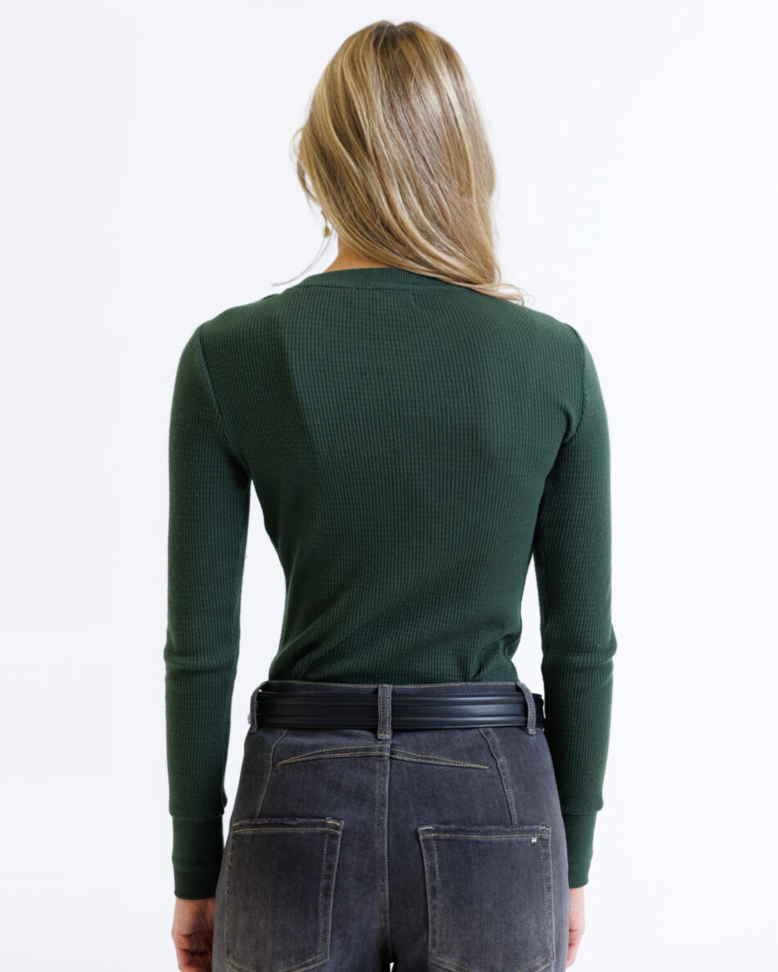 Woman wearing a green long-sleeve top and dark jeans on a white background