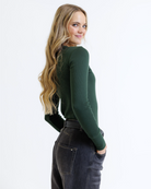 Woman wearing a green long-sleeve top and dark jeans on a white background
