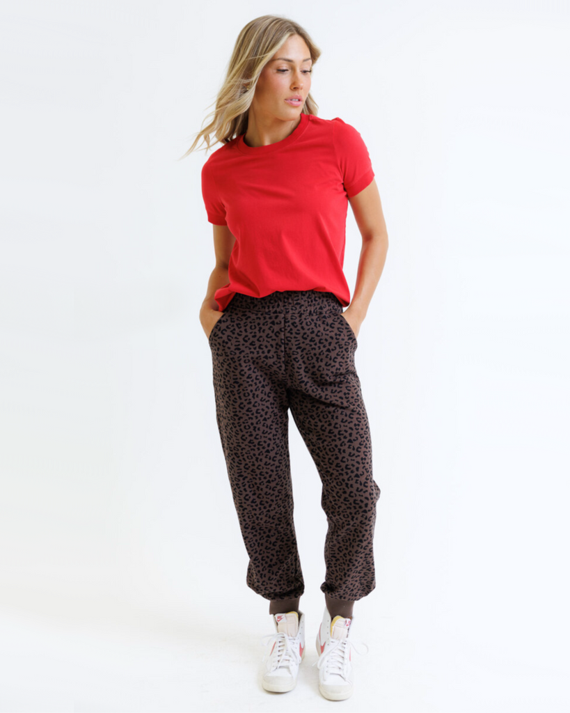 Woman wearing a red shirt and animal printed sweatpants on a white background