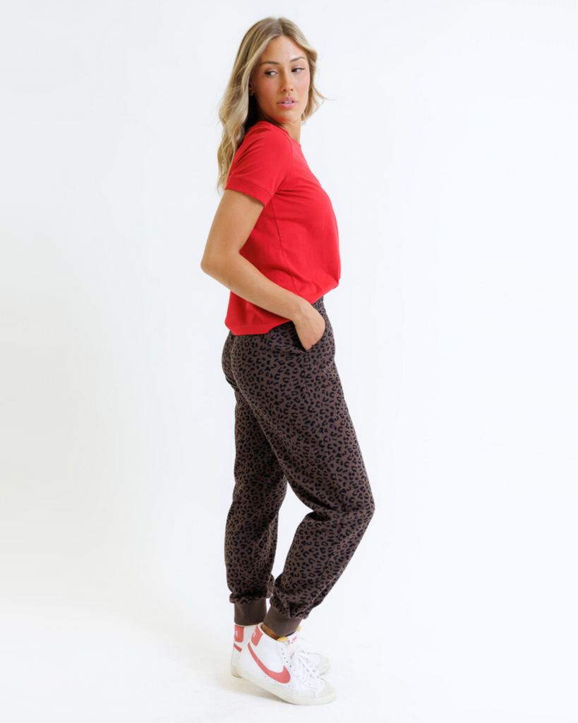 Woman wearing a red shirt and animal printed sweatpants on a white background