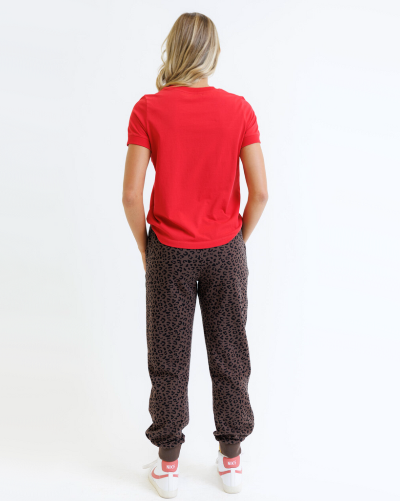 Woman wearing a red shirt and animal printed sweatpants on a white background