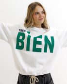Woman wearing a white sweatshirt with green text that says 'TRES BIEN' on a white background