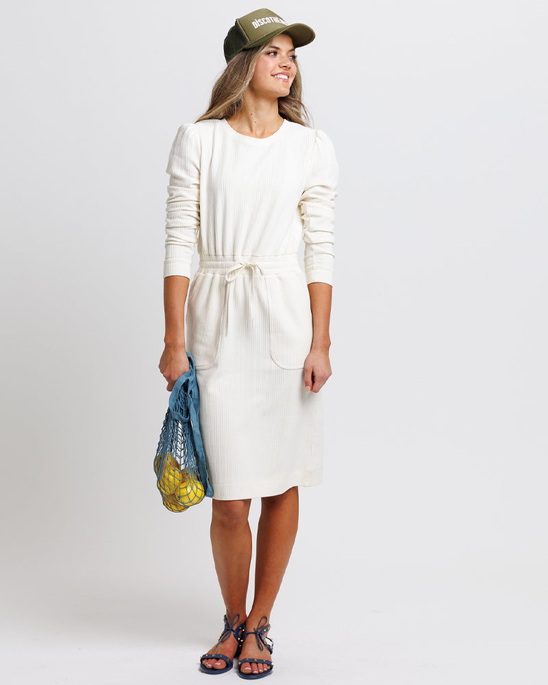 Model wearing a white long sleeve, round neck knee-length dress with a tie at the waist.
