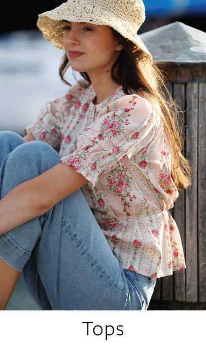 Woman wearing a floral blouse and denim jeans sitting outdoors with 'Tops' text at the bottom.