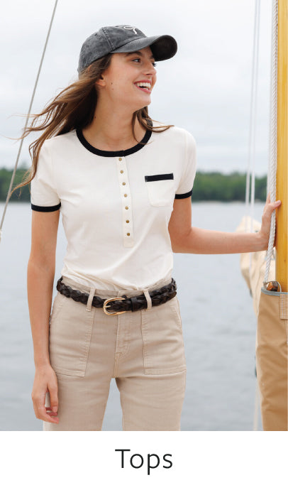 Woman wearing a white top with black trim and beige pants by a body of water.