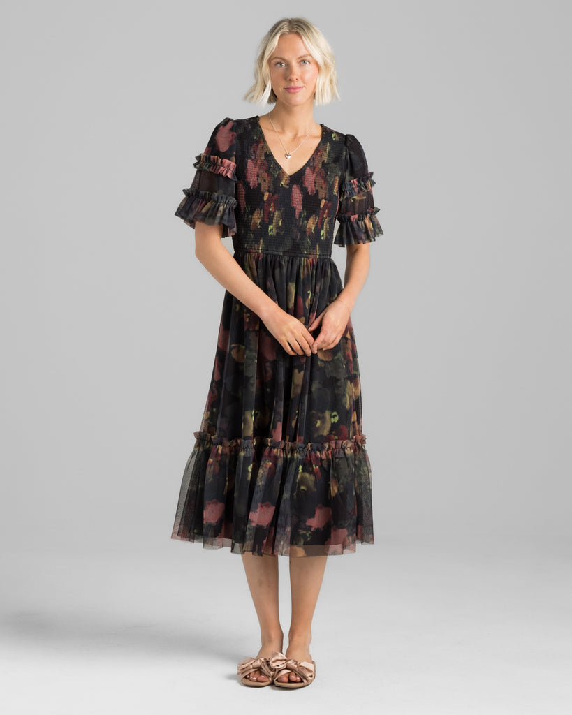 Model wearing a black with pink watercolor floral print, short sleeve with ruffles, v-neck, smocked bodice, midi length tulle dress.