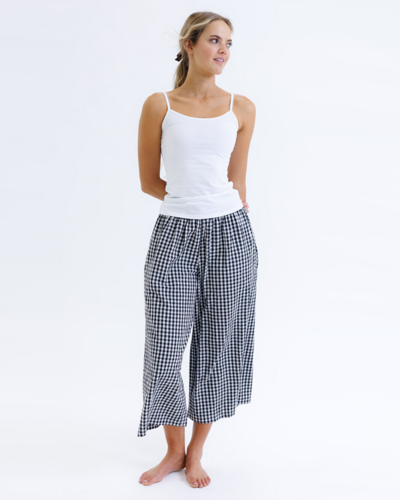 Woman wearing a white layering tank top and black and white checkered pants on a white background