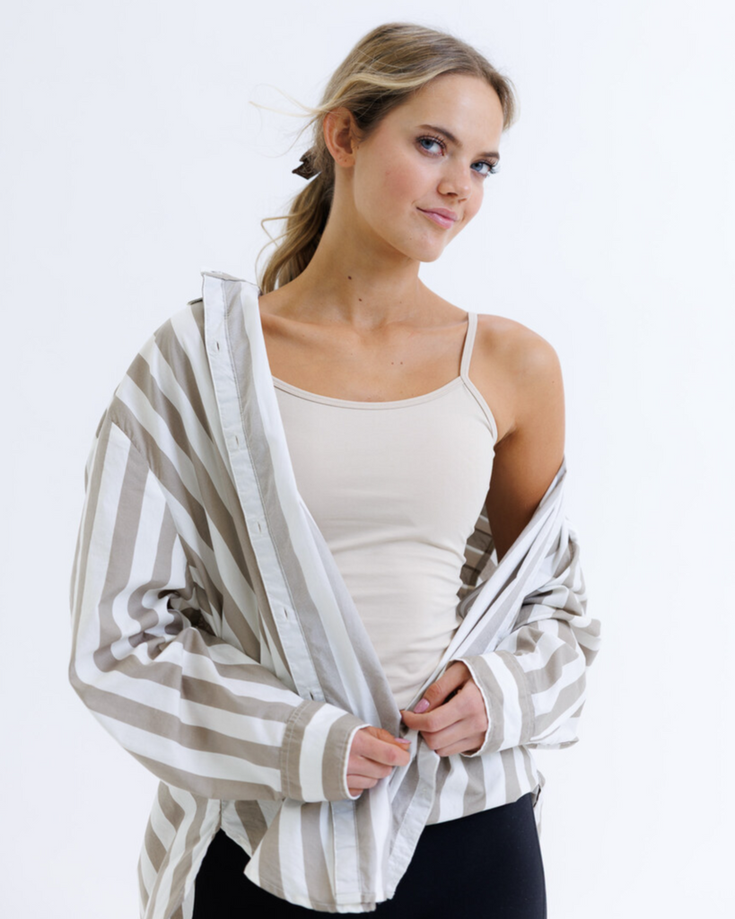 Woman wearing a striped button down over a beige camisole top on a white background