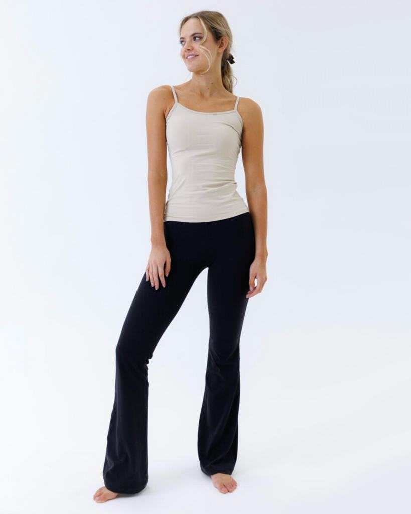 Woman wearing a beige tank top and black pants on a white background