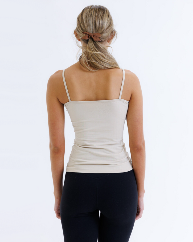 Woman wearing a beige tank top and black leggings on a white background