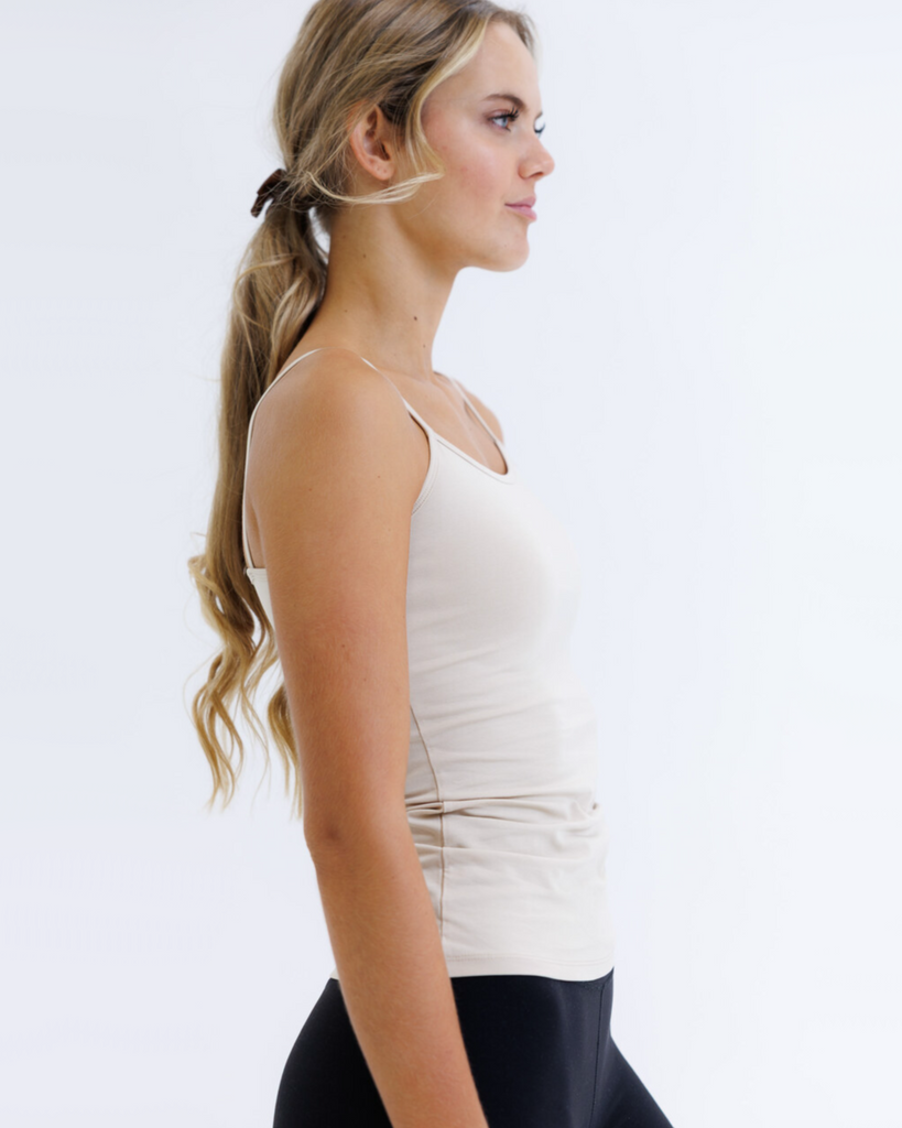 Woman wearing a beige tank top and black leggings on a white background