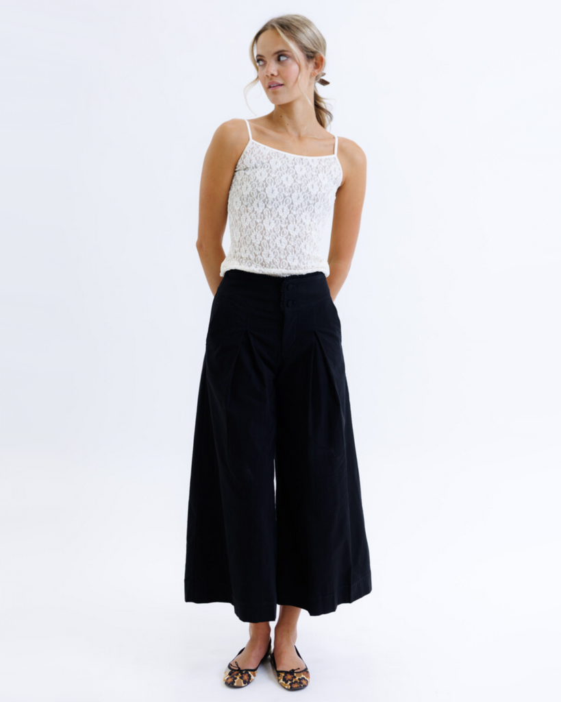 Woman wearing a white lace top and black pants on a white background