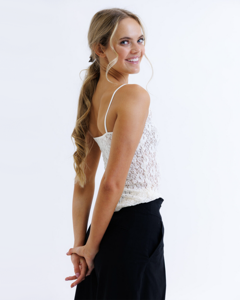 Woman wearing a white lace top and black pants on a white background