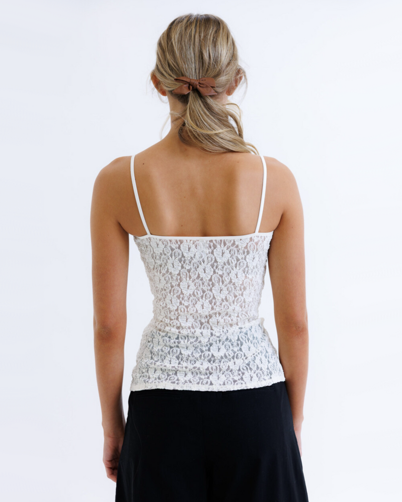 Woman wearing a white lace top and black pants on a white background