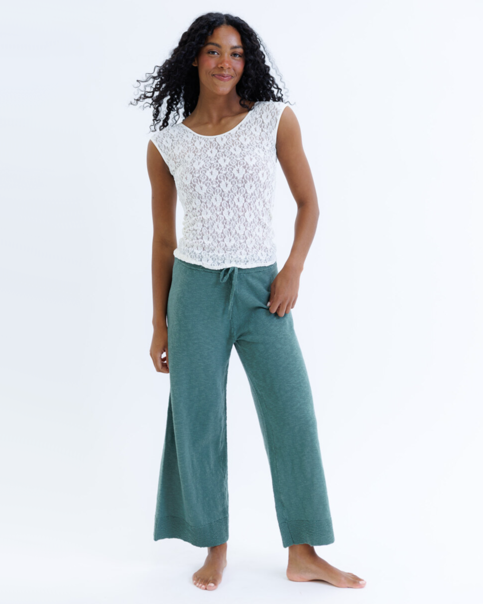 Woman wearing a white cap sleeve top and green pants on a white background