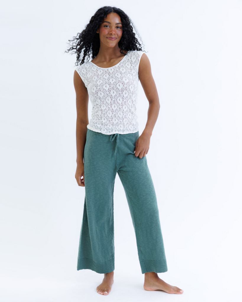 Woman wearing a white cap sleeve top and green pants on a white background