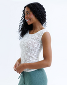 Woman wearing a white cap sleeve top and green pants on a white background
