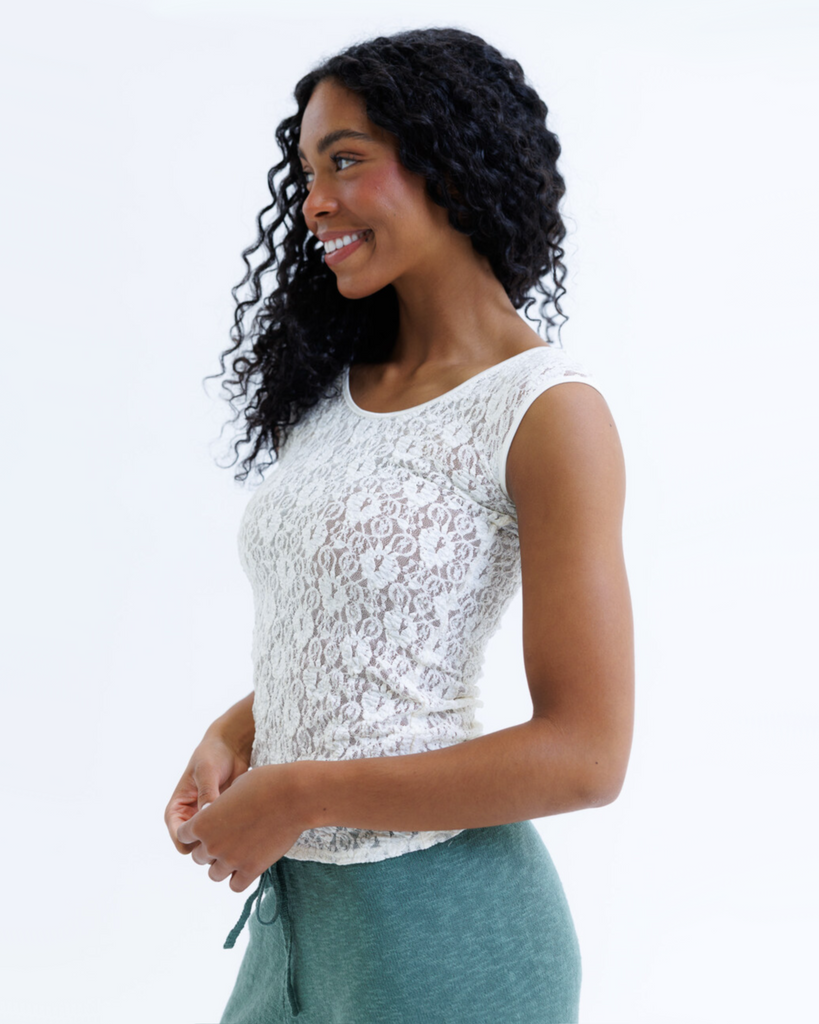 Woman wearing a white cap sleeve top and green pants on a white background