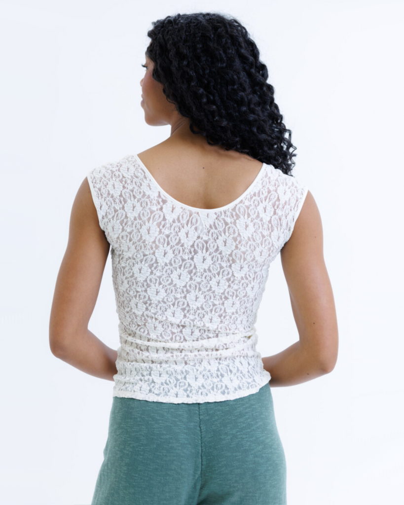 Woman wearing a white cap sleeve top and green pants on a white background