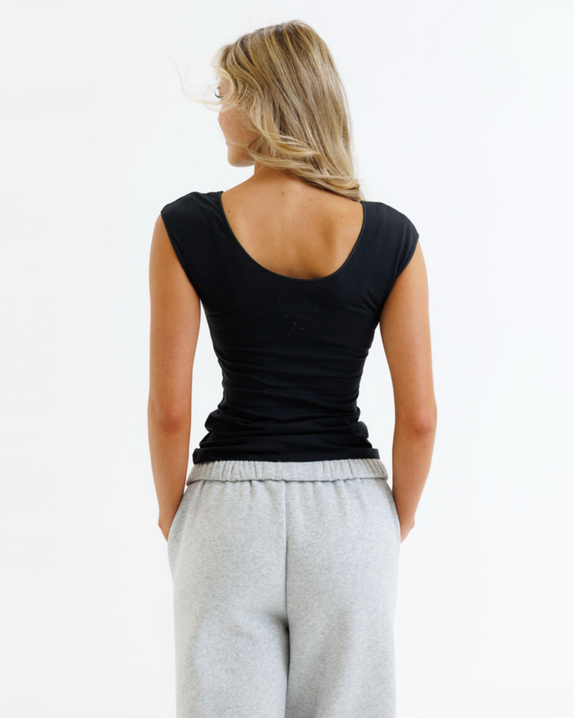 Woman wearing a black layering top and gray sweatpants on a white background