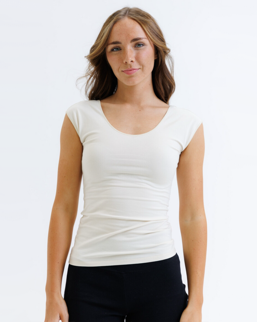 Woman wearing a cream colored layering top and black pants on a white background