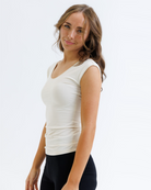 Woman wearing a cream colored layering top and black pants on a white background