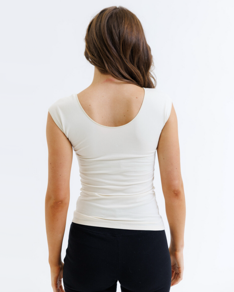 Woman wearing a cream colored layering top and black pants on a white background