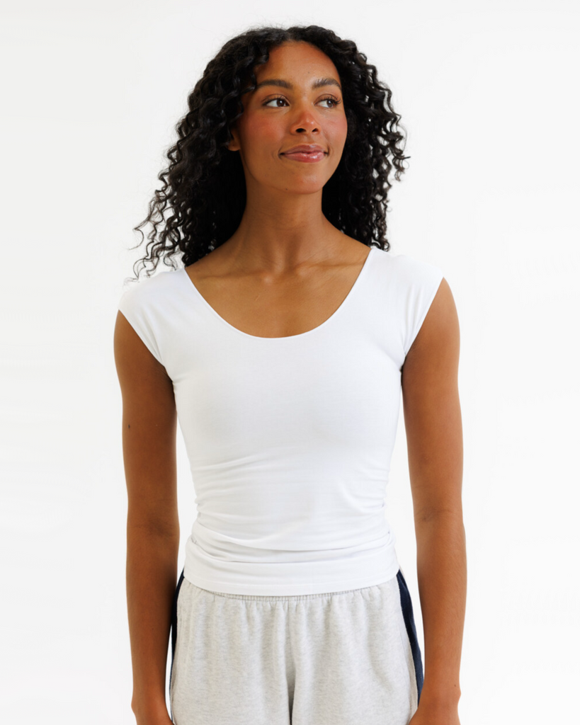 Woman wearing a white layering top and gray pants on a white background