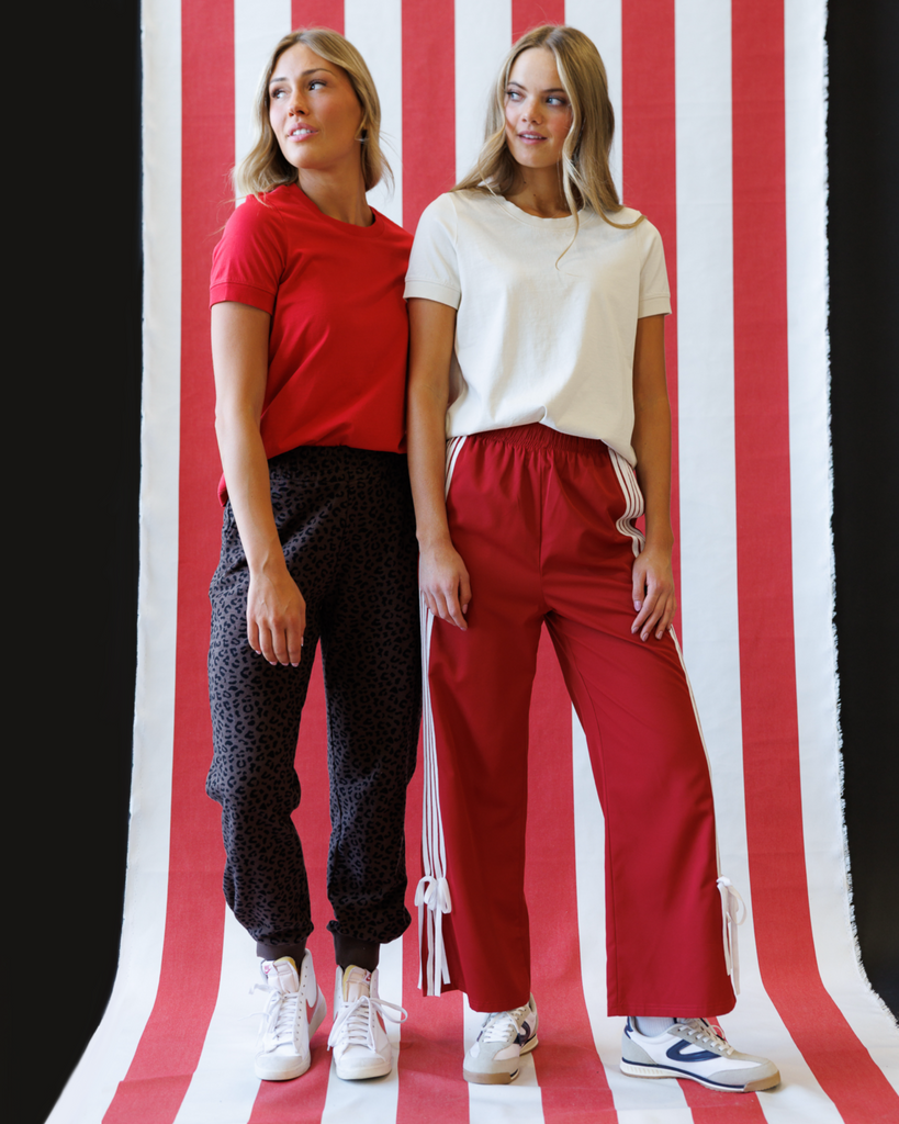 Two women standing side by side against a red and white striped background.