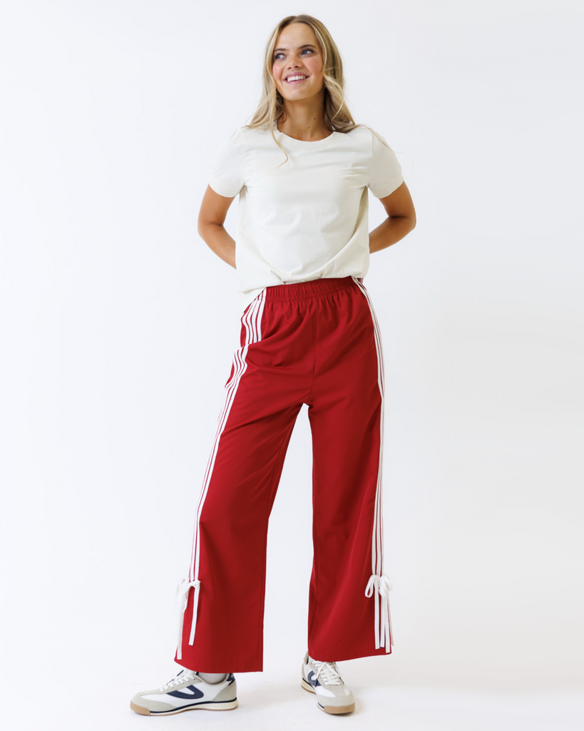 Woman wearing a white t-shirt and red track pants with white stripes on a white background