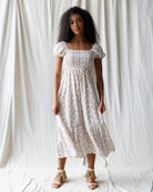 Woman wearing a white floral dress against a plain background